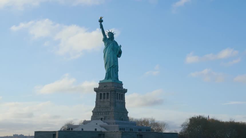 The statue of liberty stands tall as clouds move across the sky