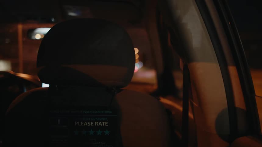 Taxi travels at night with a rating sign attached to the back of the passenger seat