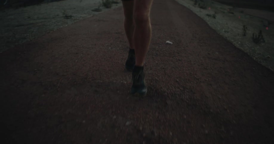 A man wearing shorts is running on a dirt road and there are mountains in the distance