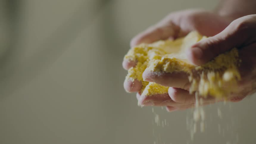 A man holding ground yellow powder in his hands sifting and feeling it then dropping it into a container