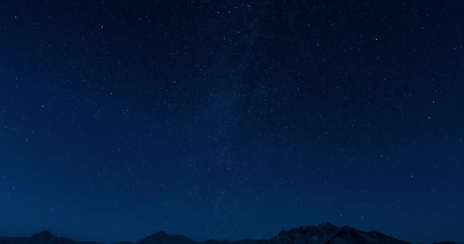 Stars move in the night sky above mountains