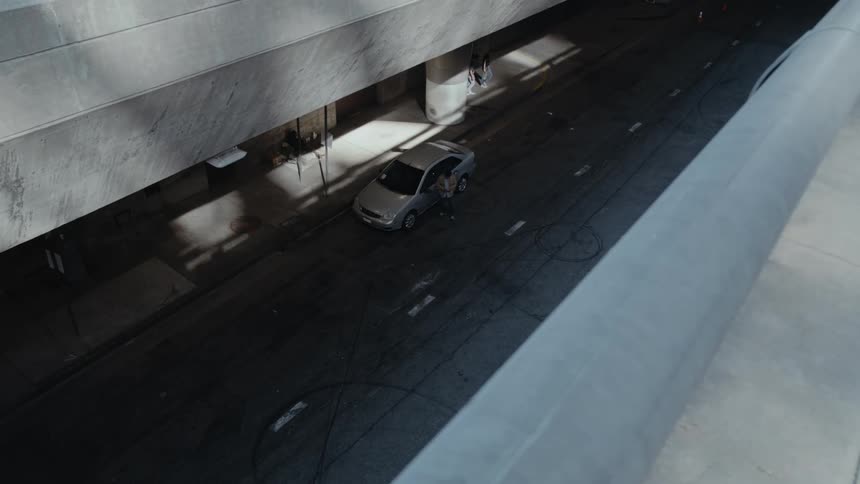 A person enters the drivers seat of a parked sedan outside of a large building
