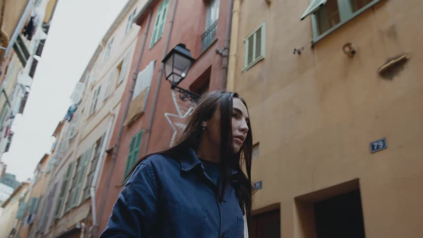 A woman looks up at the buildings as she walks down the narrow road between the homes