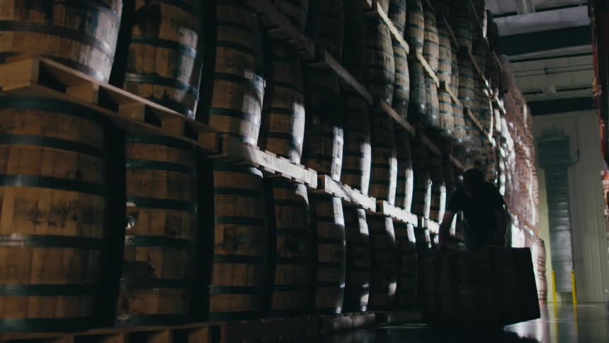 A man is moving barrels in a warehouse during midday