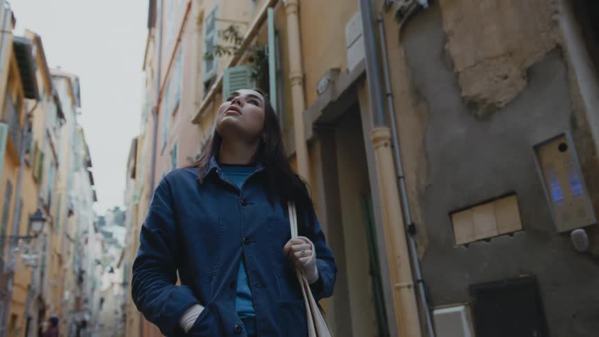 Woman with straight hair blue jacket andand brown bag walks down the street in the neighborhood