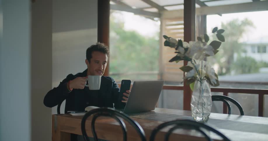 A man on his smartphone and his laptop at a table