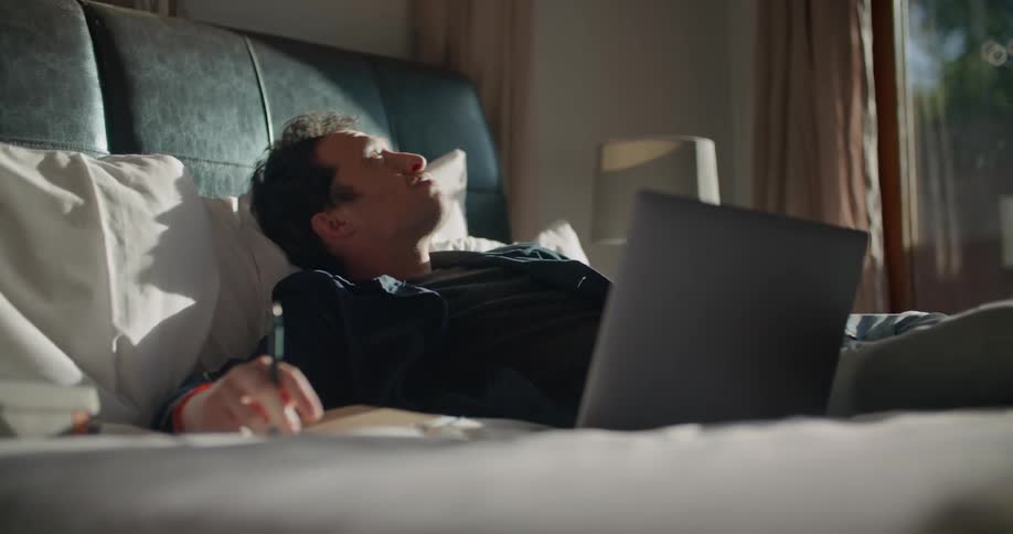 A man works from home while lying in bed with his laptop