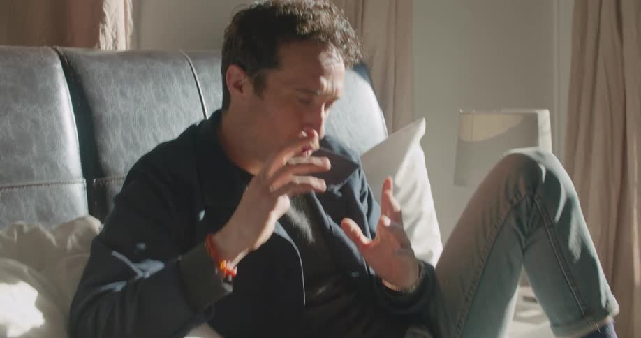 A man talks with his hand as he sits in bed during a video call on his laptop
