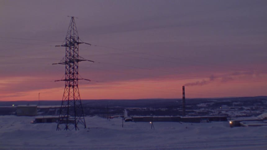 Transmission tower in front of a factory in the countryside at sunset caught on vintage film