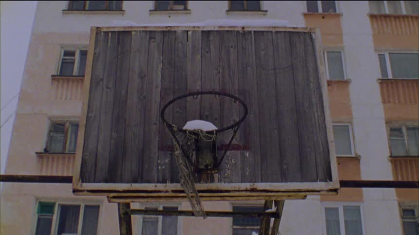 Snow falls over a basketball court in front of an apartment building