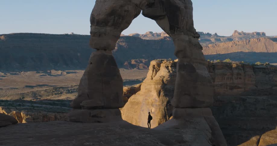 The silhouette of a hiker standing under the delicate arch in utah tilting his head back and looking up
