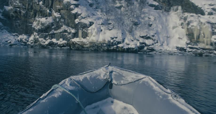 An inflatable boat sails through the ocean near snow covered mountains