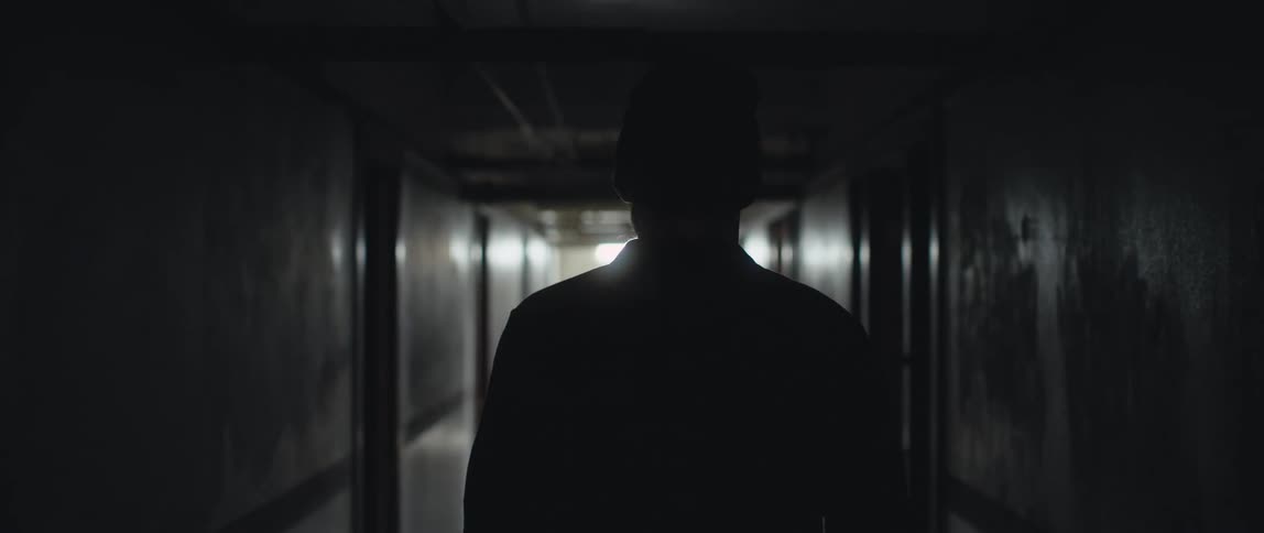 Man walks along dark corridor toward light at the end