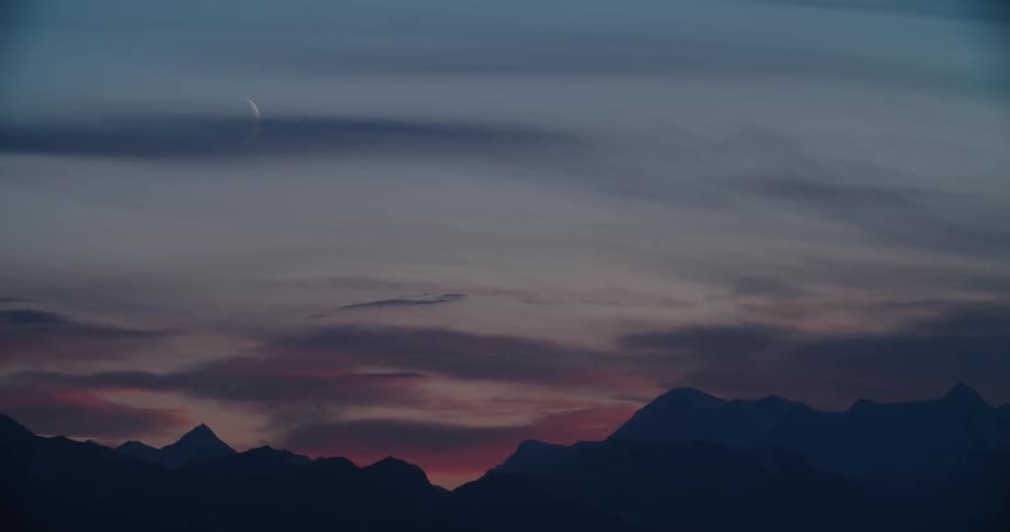 A sliver of a moon in the sky above a mountain ridge at sunrise