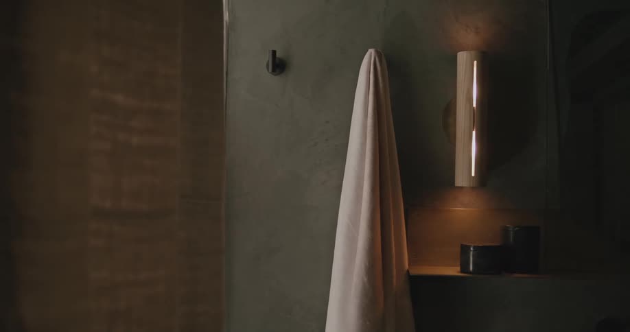 Person takes bath towel off hook on the wall in the bathroom