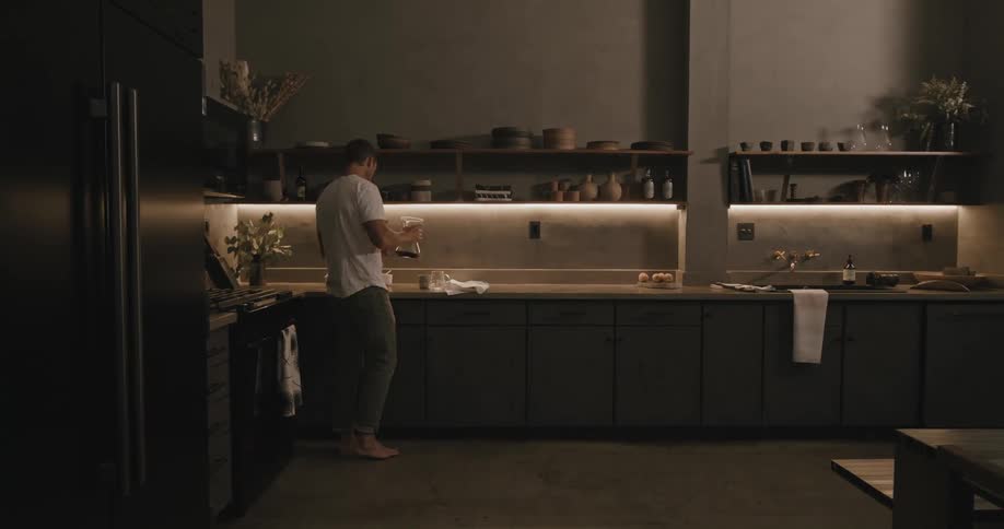 Man with white t shirt and jeans pours a cup of coffee in the kitchen