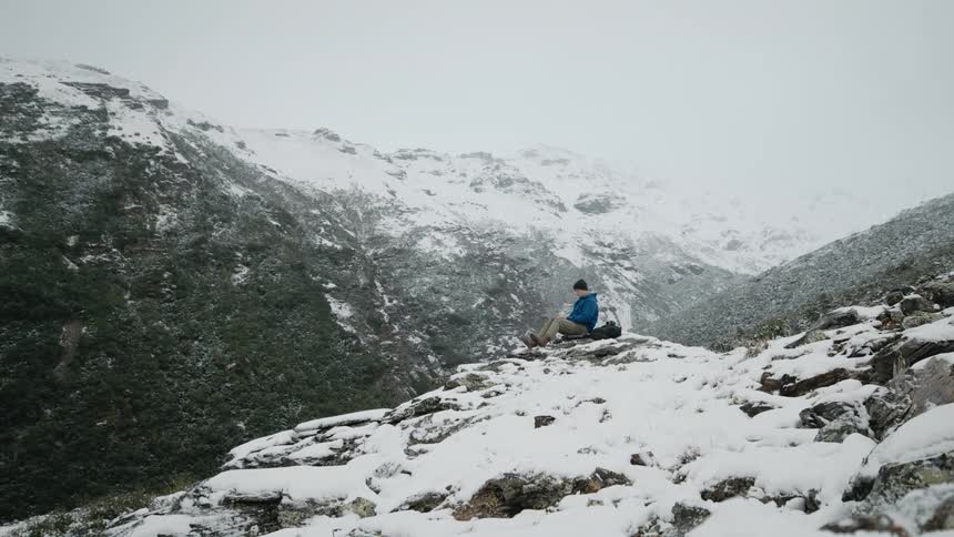 Man sitting over the rocks on the slopes of a mountain covered in snow at winter
