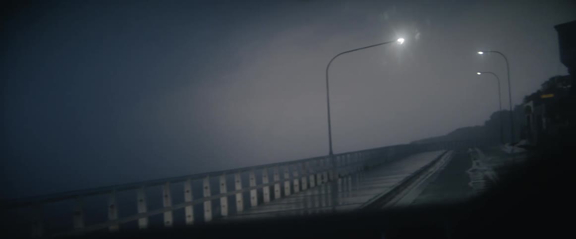 Windshield wipers move across a windshield as a car drives down a rainy street on the coast
