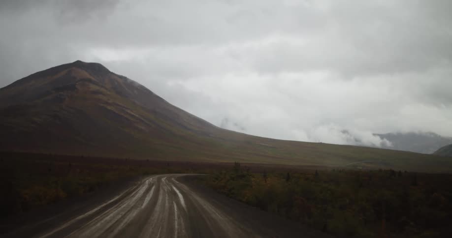Windshield wipers wipe the raindrops on a windshield as a vehicle travels towards a mountain on a rainy day