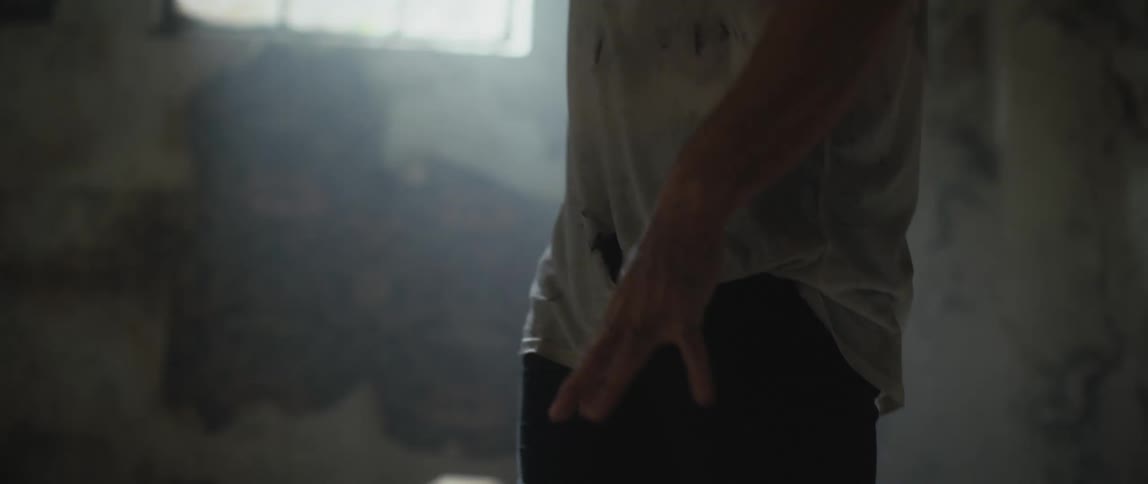 A man wearing a dirty shirt is walking in a dilapidated room