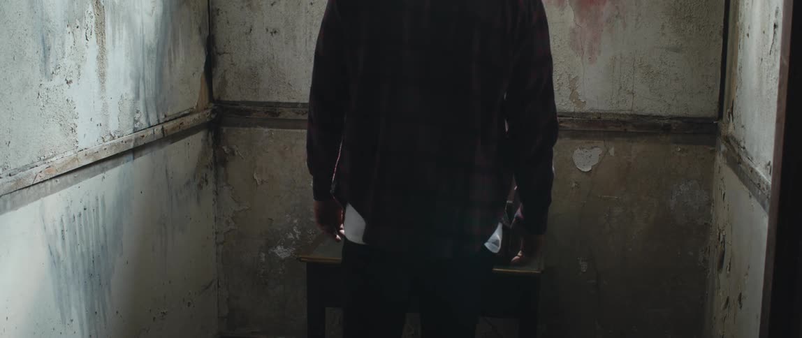 A man walks toward a record player playing an album in a dilapidated room then walks away