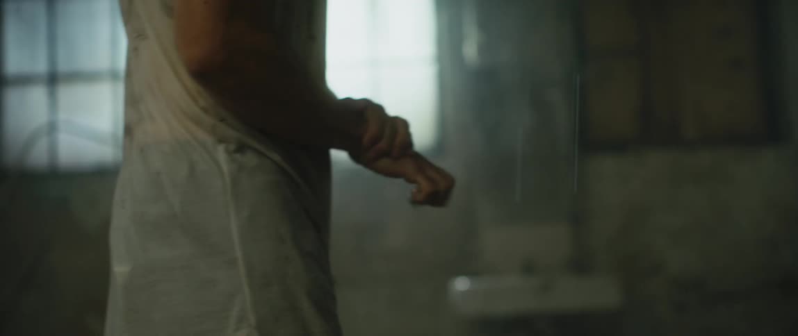 A man paces in a dirty abandoned building clenching his fingers looking like he wants to crawl out of his skin