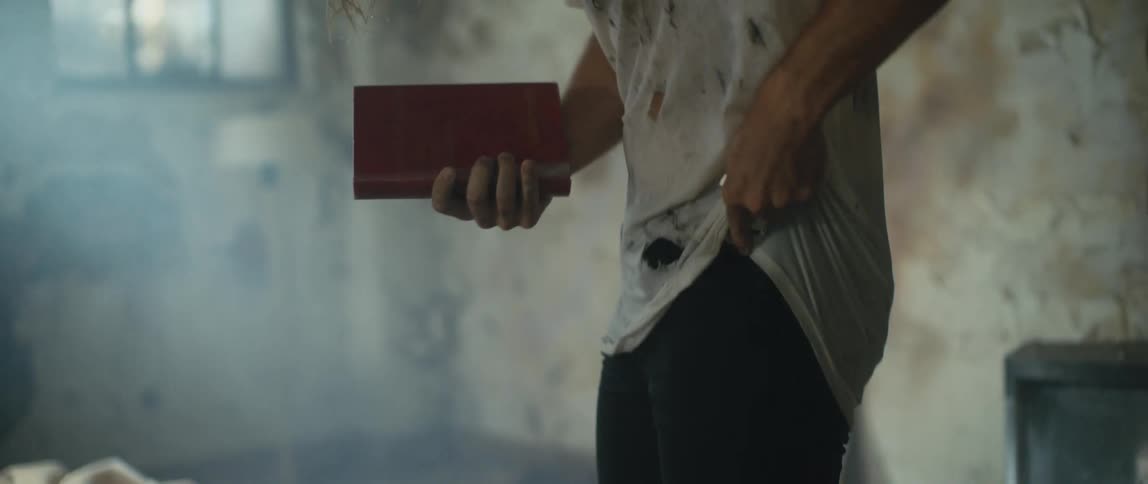 Disheveled scruffy man inside the room of an abandoned building tearing pages of a book