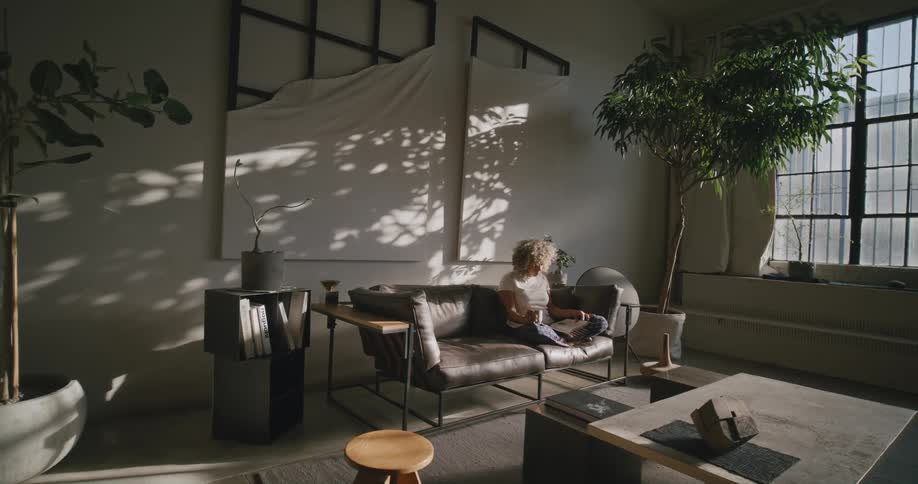 A woman sits on a couch at home and reads a magazine