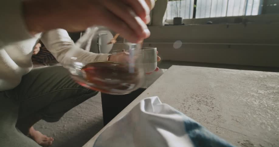 Man pours coffee into cup cleaning up spill as woman sits and reads nearby