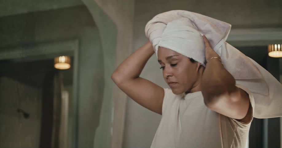 Woman with white t shirt wraps towel around her head in bathroom