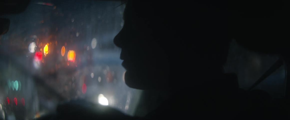 A man driving a car on a city street on a rainy night looking to his left