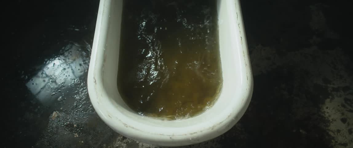 A man submerged in a tub full of dirty water sits up suddenly