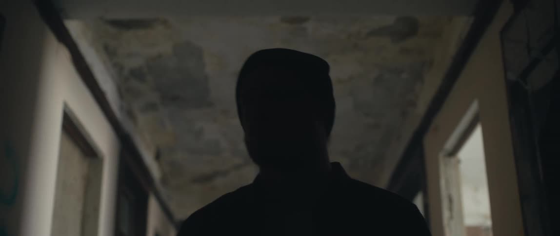 A man wearing a knit cap is walking down a hallway and looking around in a suspicious manner