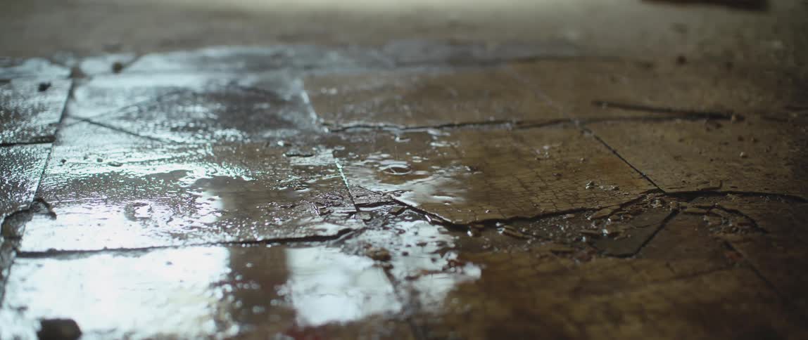 Water droplets leaking from the ceiling over the broken tiles on the floor of an abandoned building