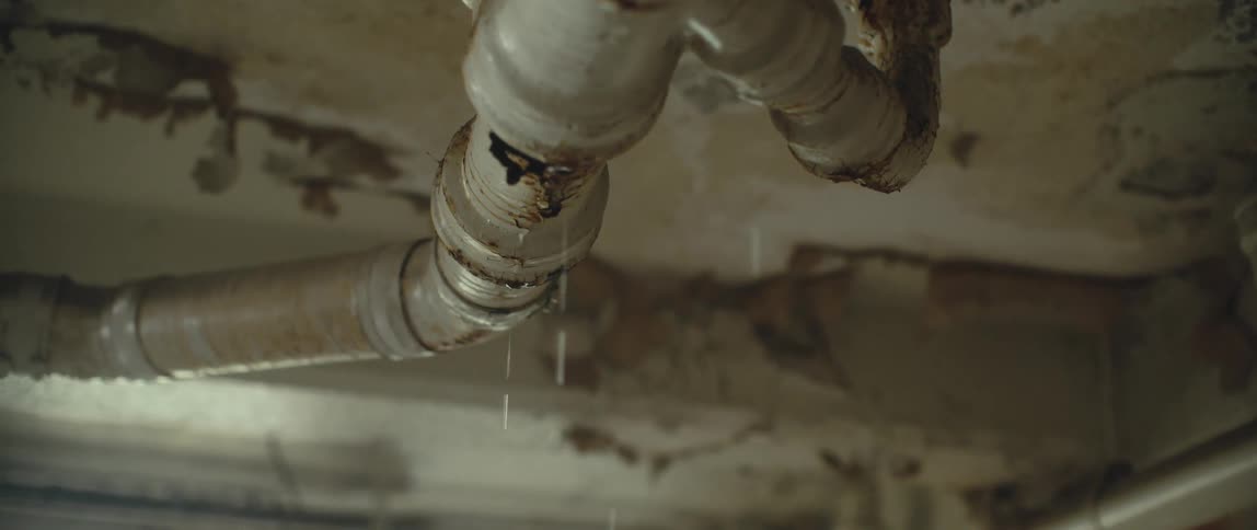 Water drips from rusty pipes that are near the ceiling and peeling paint