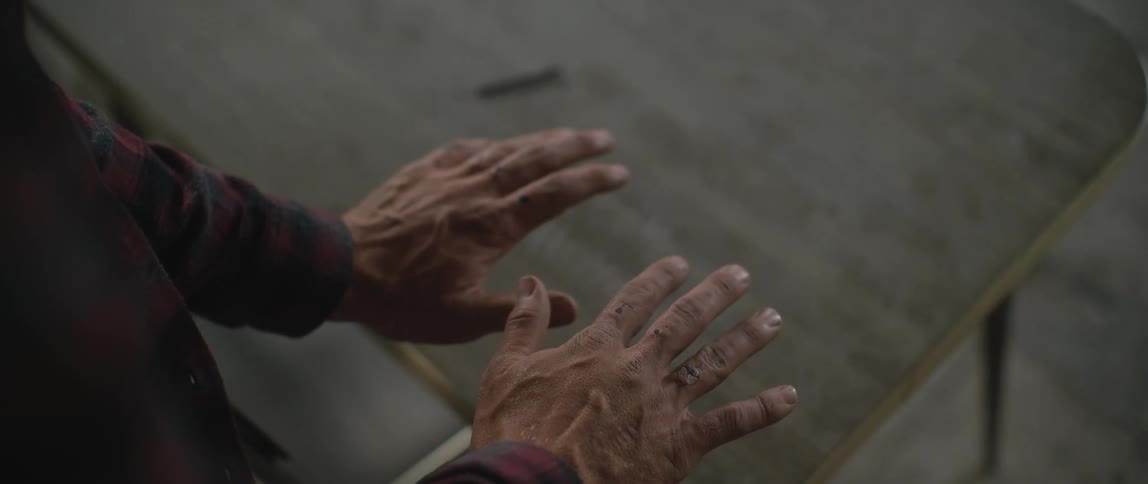 A man caresses the surface of an old school desk that has welcome home scratched into it
