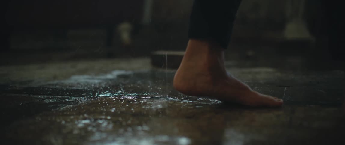 Someone walks across the floor of an old building in bare feet as water drips on the floor