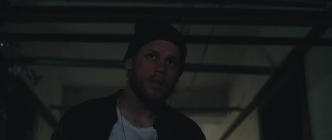 Man with black wooly hat jacket and white shirt walks along the hall in old building