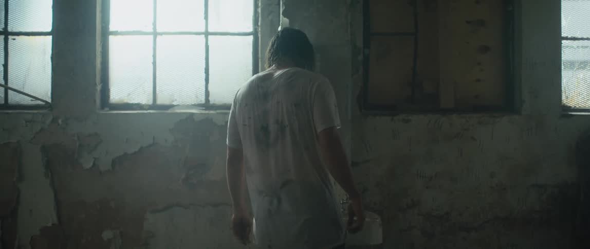 A man covered in dirt in a filthy room walks up to a sink and shakes his body and starts pounding on the wall in rage
