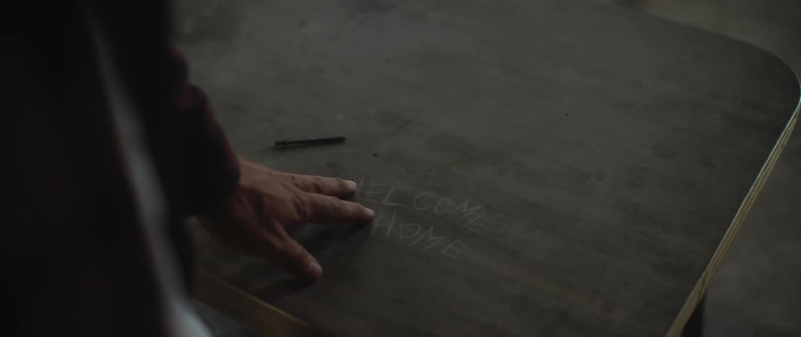 Person touches wooden school desk engraved with the message welcome home