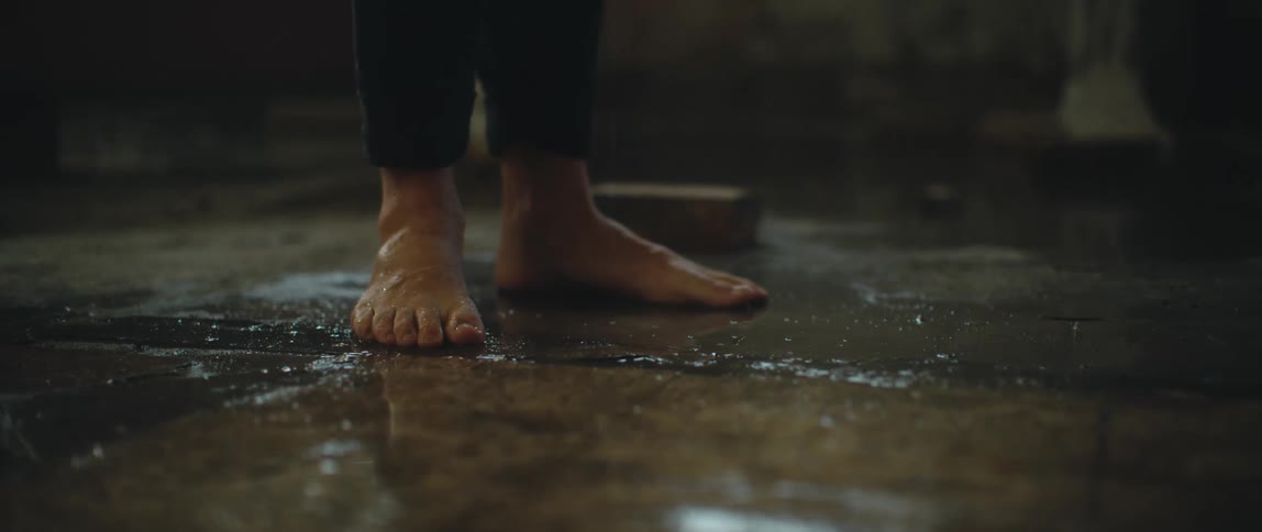 Barefoot man walks over a concrete floor wet with water coming from leaks on the ceiling