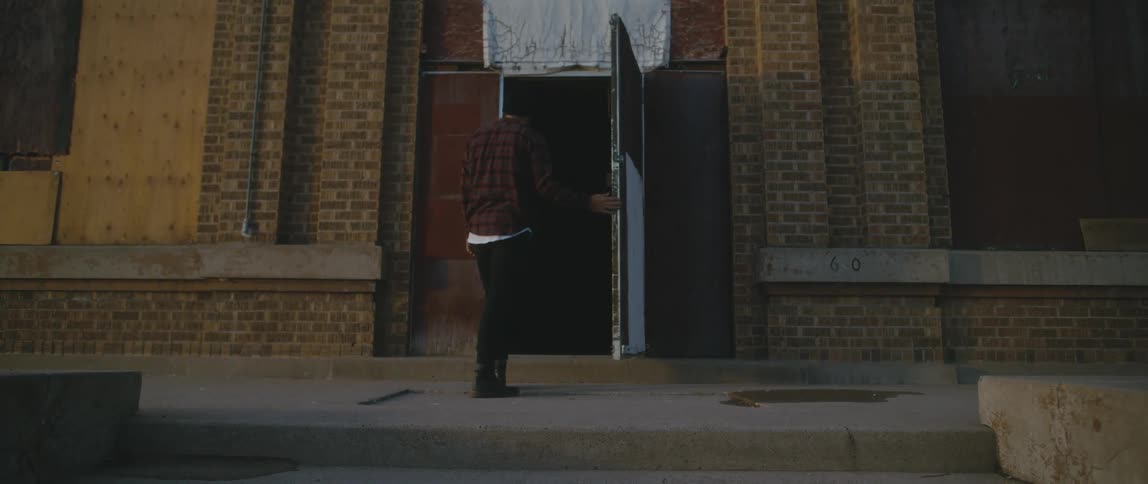 Young man slowly walks up the stairs to a building entrance before opening the door and stepping in