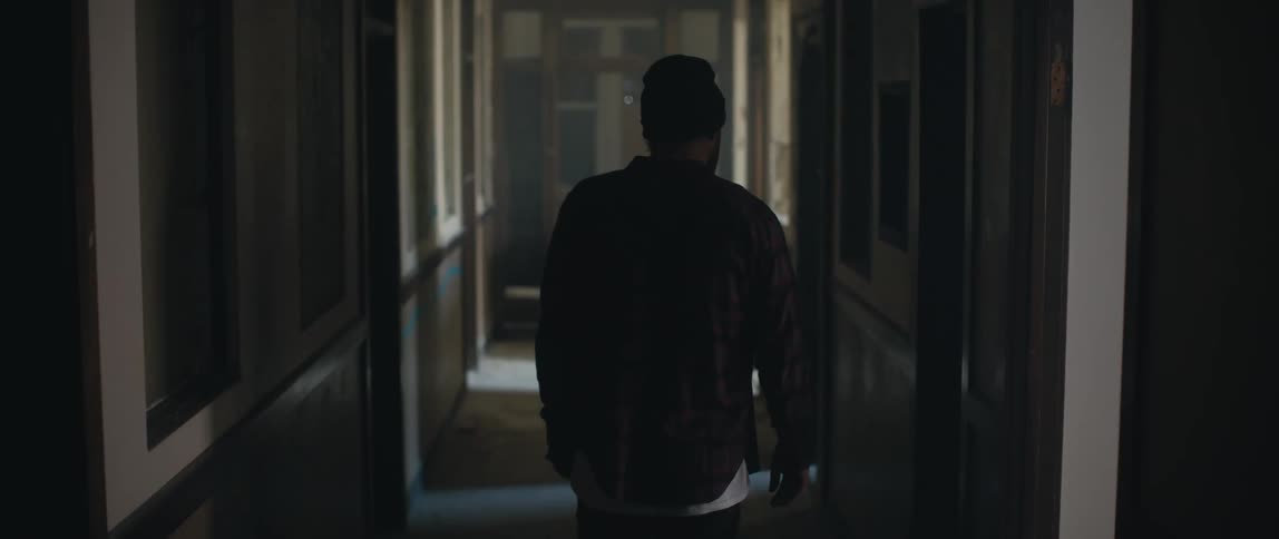 Man with wooly hat and black jacket walks along hall in old building
