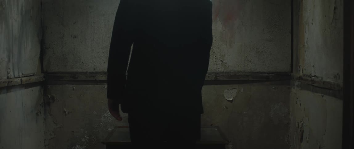 A man turns on a record player in a room with soiled walls