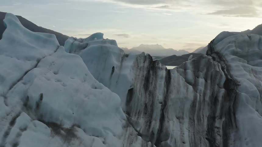 An iceberg is melting in the water and there are mountains in the distance