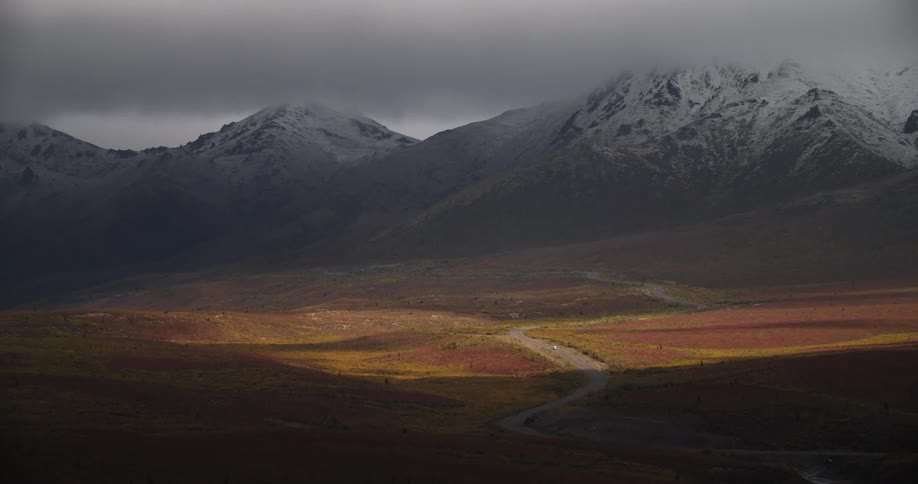 Vehicle moves along winding road from misty snow covered mountains and through red and yellow colored fields