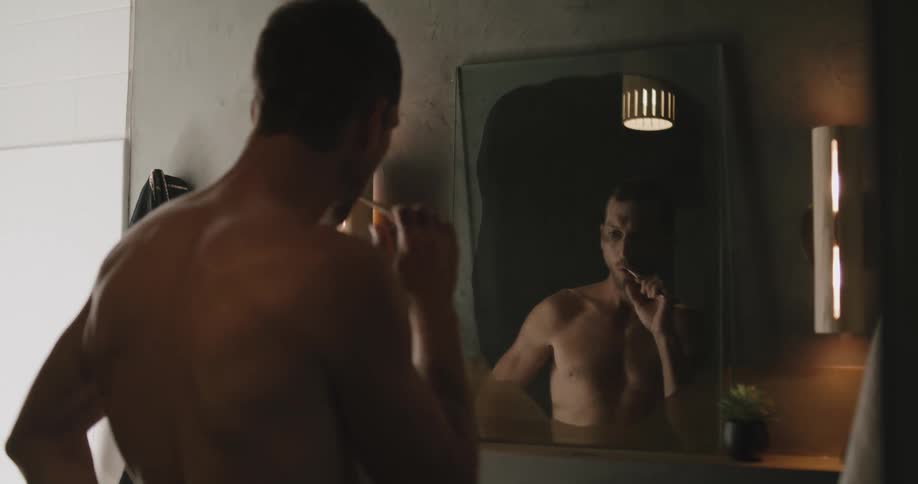 Shirtless man brushes his teeth with toothbrush in the bathroom