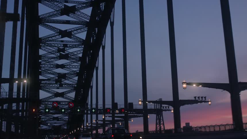 Traffic moves over bridge as buildings stand against red horizon