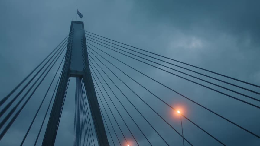A flag flies on top of a suspension bridge under a cloudy sky