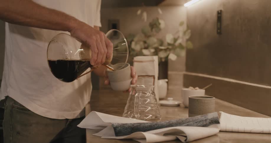 Man with white t shirt and jeans pours a cup of coffee in the kitchen